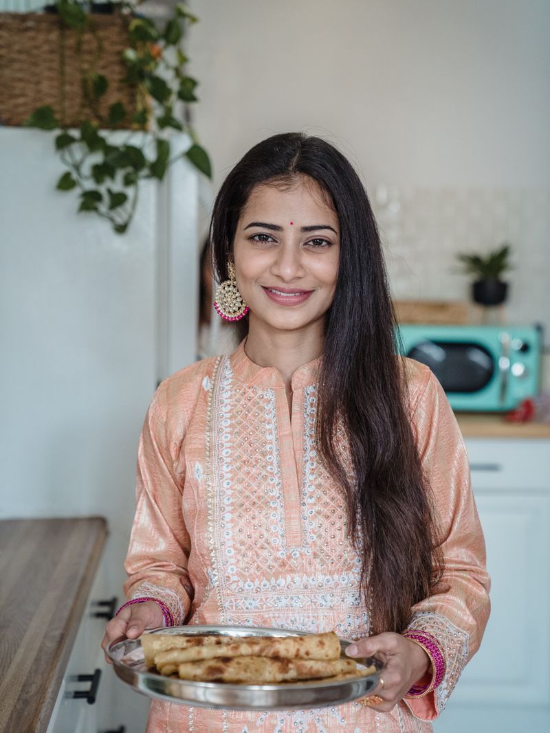 Representative portrait — Indian woman wearing traditional clothing holding a tray with food indoors.
