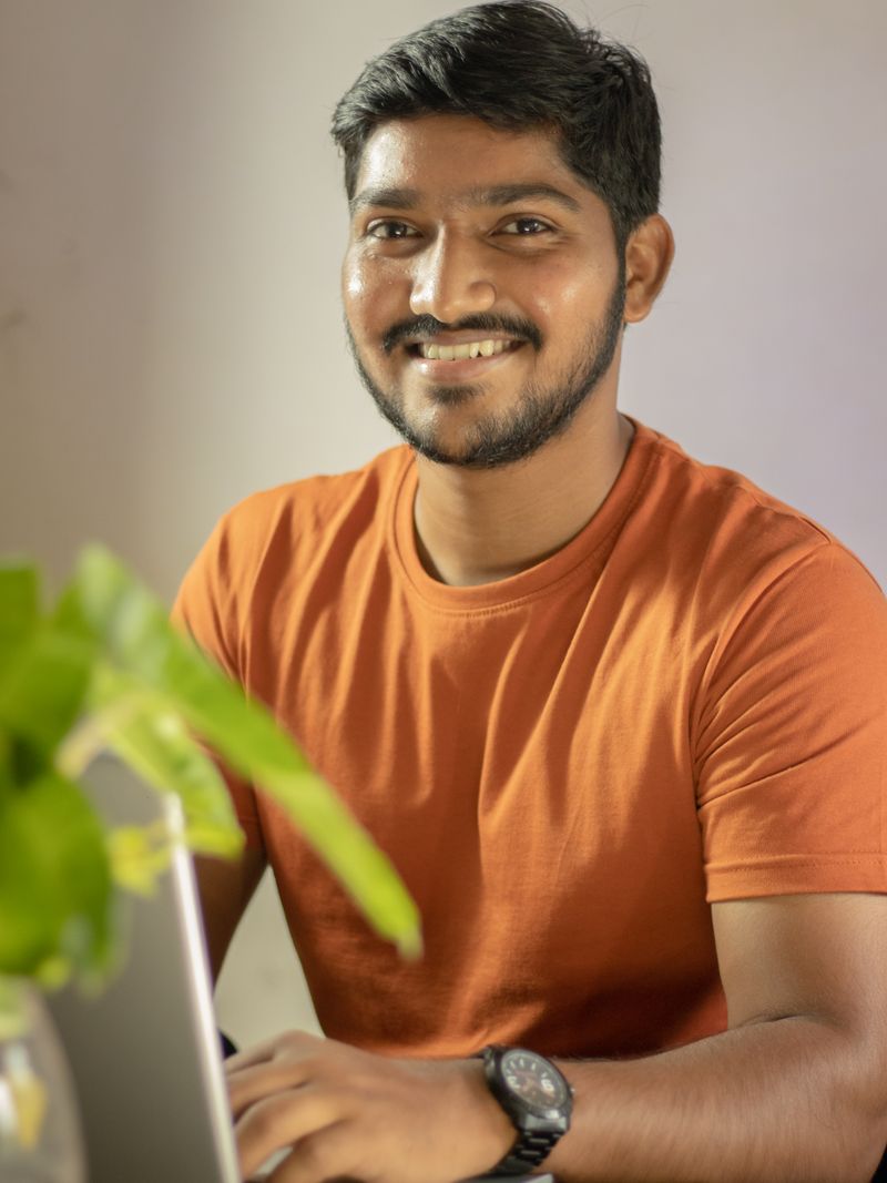 Representative portrait — Man in an orange shirt enjoying remote work from home setup with a laptop.