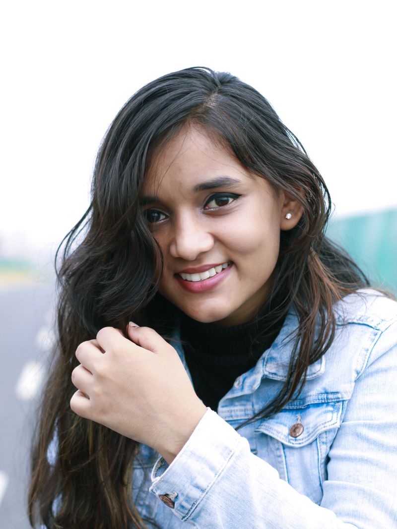 Representative portrait — Close-up portrait of a smiling young woman in a denim jacket outdoors.