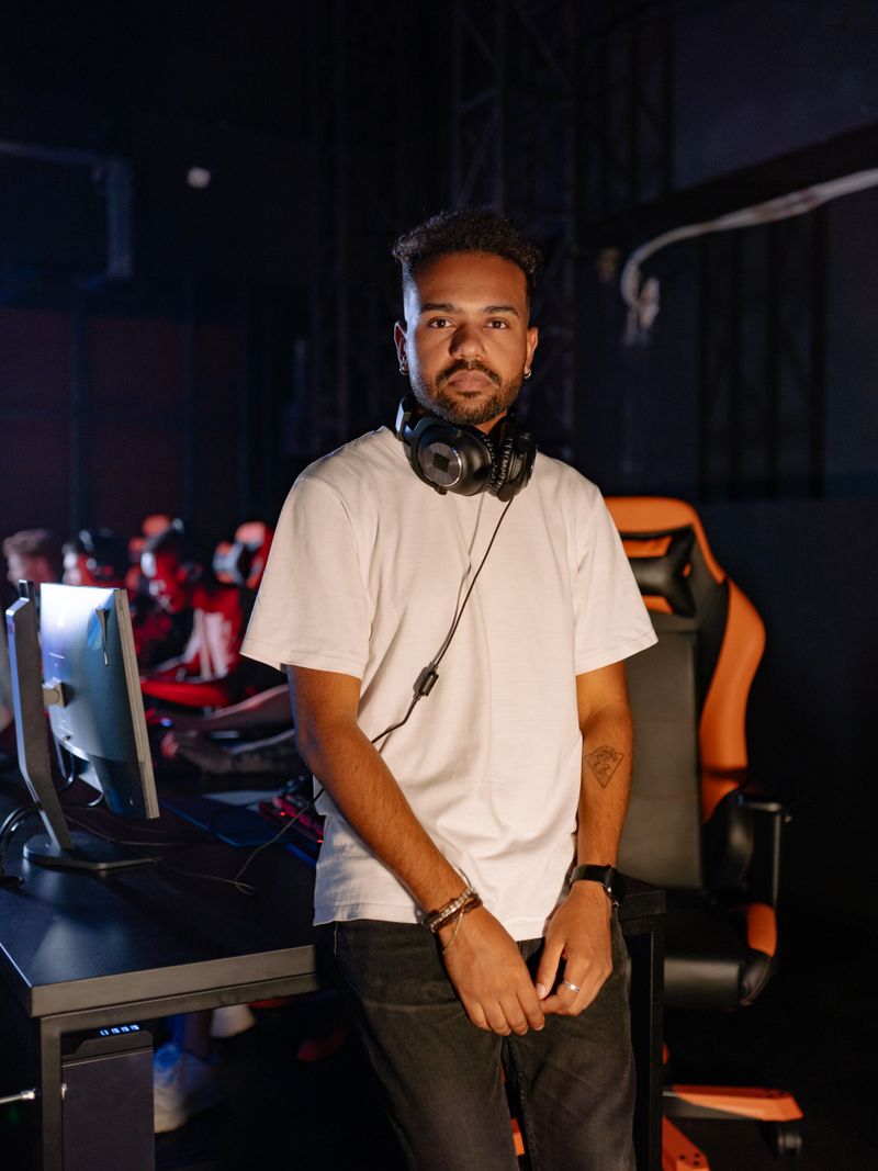 Representative portrait — Young man standing in an esports room with a computer, engaged in gaming. Indoors with headphones.