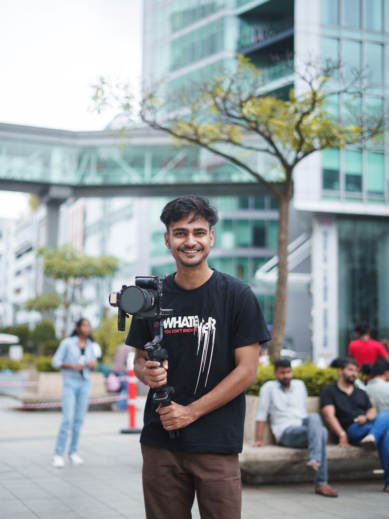 Representative portrait — A young filmmaker smiling while holding a camera in a vibrant urban setting.