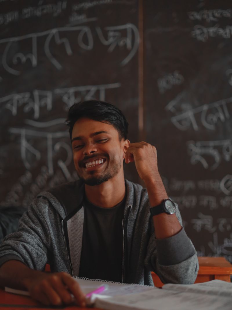 Representative portrait — Young South Asian student smiling in front of a chalkboard in a Bangladeshi classroom.