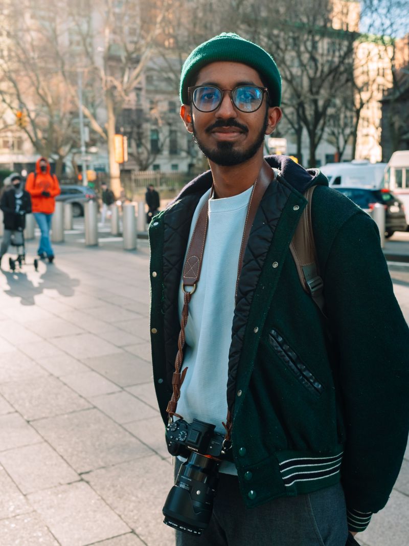 Representative portrait — Street portrait of a smiling South Asian photographer with a camera outdoors.
